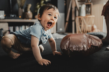 Cheerful child on the floor, smiling and full of energy, next to a copper balloon, in a warm, home environment