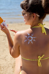 Woman applying sunscreen cream on tanned shoulder in the form of the sun. Skincare. Body Sun...