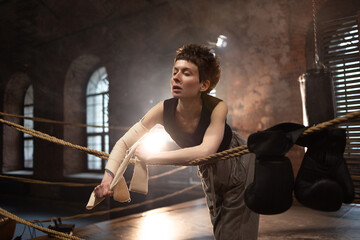 A woman in a boxing ring, wrapping an elastic bandage around her arms, preparing for boxing...