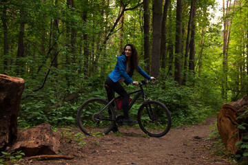 Beauty smiling sport free woman biking on bicycle on path with logs in green woods in a summer...