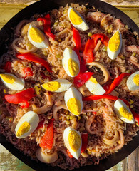 Delicious seafood paella with boiled eggs, squid, and red bell peppers being cooked in a pan