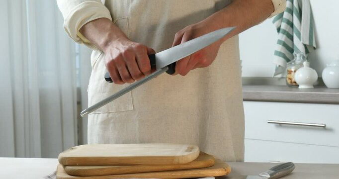 Man sharpening knife with sharpener at beige table indoors, closeup