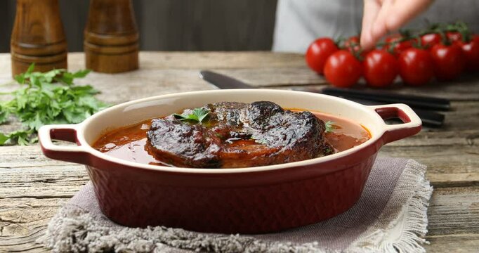 Woman putting traditional ossobuco dish onto wooden table, closeup