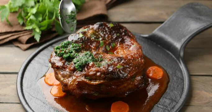 Woman adding pesto sauce to traditional ossobuco dish at wooden table, closeup