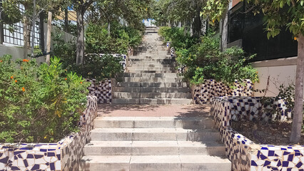 Stone steps surrounded by greenery lead to an elevated pathway in a cheerful urban setting during daylight hours
