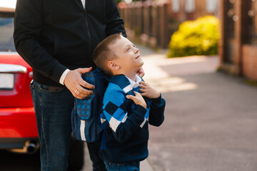 Father supports son with backpack before school, happy child looking up, first day back to school