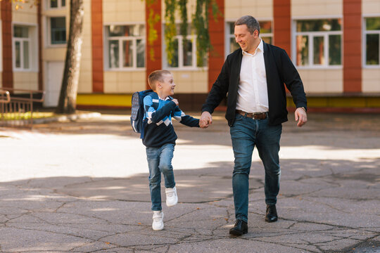 Father and son walking to school together, happy boy with backpack, first day back to school, outdoors