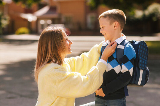 Mother preparing smiling son with backpack for first day of school, morning, back to school concept