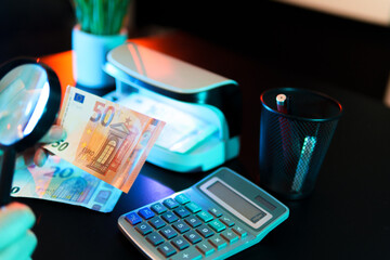 Cashier verifying authenticity of euro banknotes with magnifying glass and currency detector