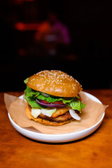Juicy hamburger with lettuce, tomato, onion, cheese, and a sesame seed bun served on parchment paper in a white plate. Classic American fast food with a gourmet twist