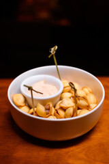 Golden fried dumplings with meat filling served in a white bowl with dipping sauce and skewers. A...
