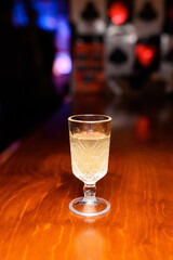 Elegant shot glass with a light cocktail on a wooden bar counter in a nightclub. Colorful blurred lights create a festive and cozy nightlife atmosphere