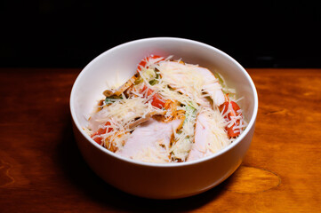 Fresh Caesar salad with grilled chicken, cherry tomatoes, romaine lettuce and grated parmesan in a white bowl on a wooden table