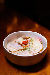 Fresh Caesar salad with grilled chicken, cherry tomatoes, romaine lettuce and grated parmesan in a white bowl on a wooden table