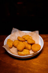 Golden crispy chicken nuggets served on parchment paper in a white plate on a wooden table. Tasty fast food snack, perfect for parties or quick meals