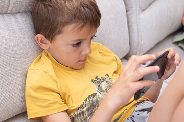 Child engaged with mobile device while sitting on a couch, exhibiting poor posture and a curved back