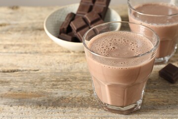 Tasty chocolate milk in glasses and pieces on wooden table, closeup. Space for text