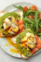 Delicious sandwiches with avocado, poached egg, salmon, tomatoes and arugula on gray table, top view