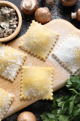 Uncooked ravioli and mushrooms on black table, closeup
