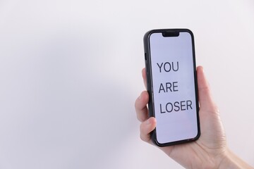 Cyber bullying. Woman holding smartphone with text You Are Loser on white background, closeup. Space for text