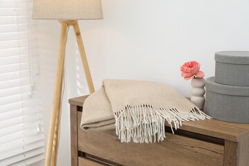Beige woolen blanket, boxes, beautiful flower in vase on wooden chest of drawers and lamp near...