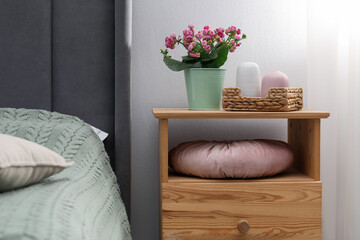 Bedside table with flowers and decor near bed indoors