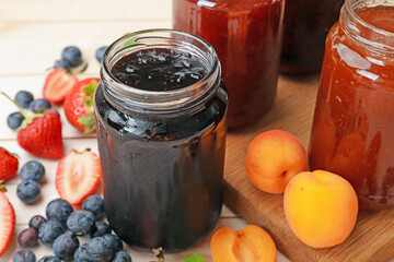 Tasty sweet jams in jars and ingredients on light wooden table, closeup