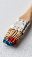 Paintbrush with blue and red paint on bristles on white surface