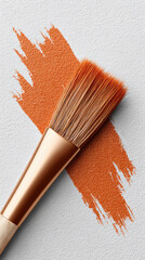 Paintbrush with orange paint stroke on textured white surface