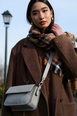 Elegant Asian woman with a stylish bag posing outdoors, looking fashionable