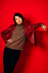 A confident person strikes a pose against a bold red backdrop. The woman is dressed in a stylish ensemble and her look exudes confidence and fashion-forward elegance