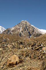 Majestic mountain peak rises above rocky terrain under clear blue sky, showcasing the beauty of...
