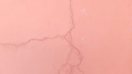 Pink concrete wall has cracks due to poor quality construction. Cracked wall surface