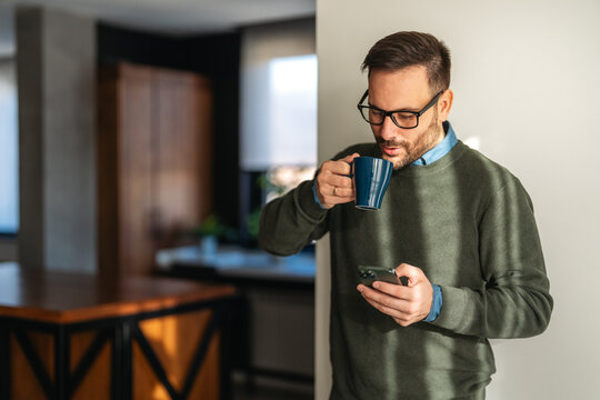 Checking his messages over coffee. Man using a smart phone while drinking coffee at home
