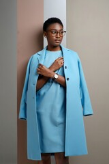 Elegant African American woman in glasses and a light blue coat posing against a multicolored background