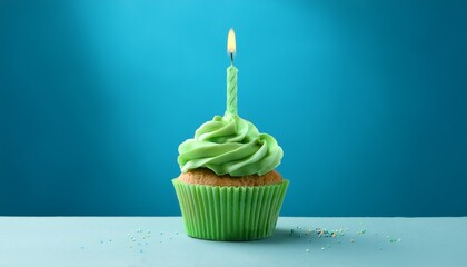 green cupcake with lit candle on a blue background