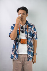 Young asian man wearing blue summer shirt is crying and feels sad, isolated over white background.