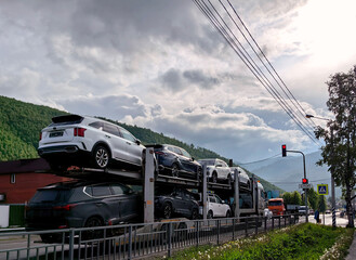 large transport truck is loaded with several vehicles, moving along scenic road near mountainous...