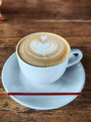 Latte art in white cup served on wooden table with red stirrer