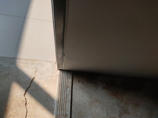 Misaligned floor joint and door gap with shadowed lighting, illustrating issues in door...
