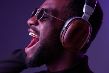Young African man enjoying music with headphones, expressing joy and passion Dark background with...