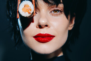 Stylish woman with sushi, vibrant red lips, and short black hair showcasing modern culinary culture...