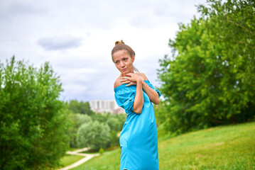 Fototapeta premium A woman in a blue dress is standing in a grassy field. She is looking at the camera with a serious expression. The scene has a peaceful and serene atmosphere, with the lush green grass