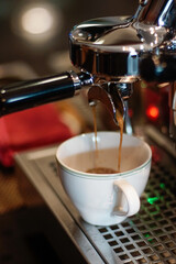 Close up of fresh espresso flows from coffee machine into a white cup