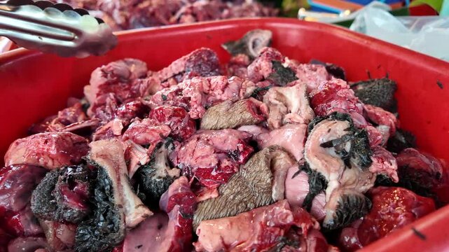 Close-up of raw mixed animal organs in a red tray, held with tongs at a local market meat