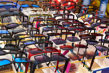 A vibrant array of stylish sunglasses is beautifully displayed in neat rows, each pair capturing the various sunlight colours and making this market stall a kaleidoscope of fashion and summer vibes.