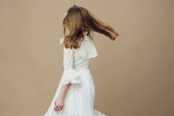 Young girl in a flowing white dress, spinning gracefully against a soft beige background,...
