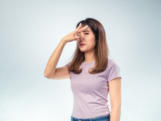 Asian woman in a purple shirt holds her nose in disgust, reacting to a bad smell with a frown and...