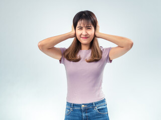 Asian woman in purple t-shirt and jeans covering her ears with both hands while squinting in...