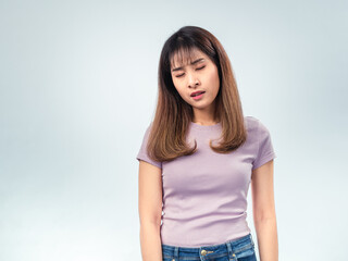 Obraz premium Asian woman in a purple t-shirt looking down with eyes closed, showing a tired or disappointed expression against a plain studio background